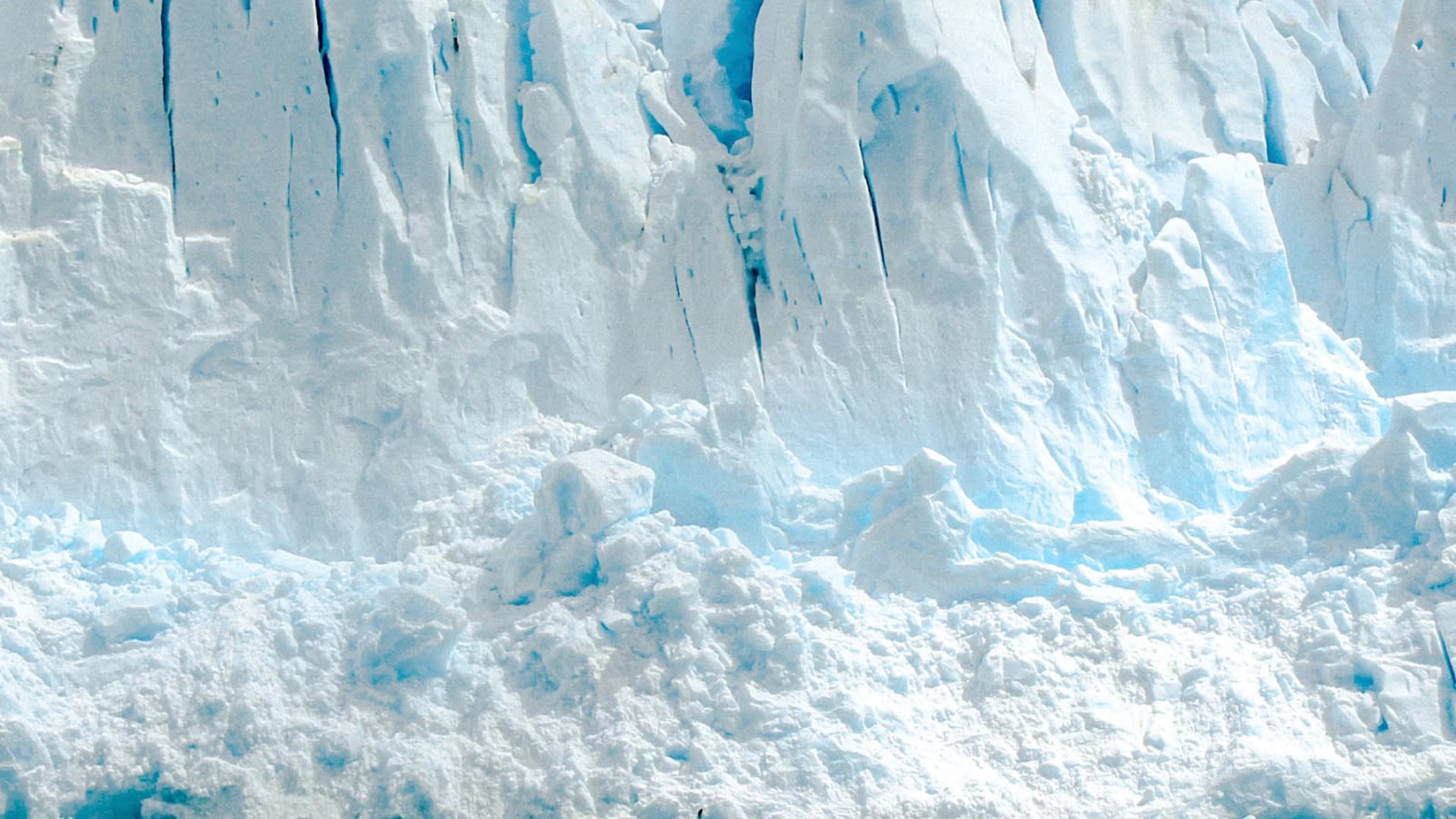Close-up of a glacier's calving face, pale blue ice cliffs above broken snow