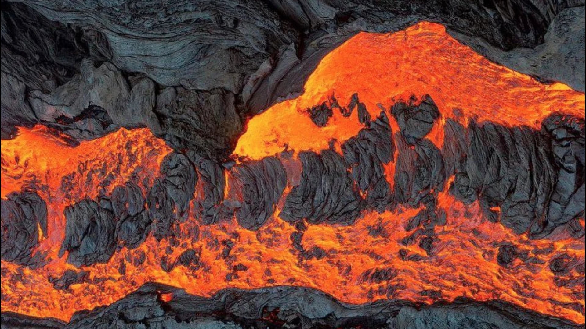 Close-up of molten lava breaking through a cooled black crust, orange seams running through dark rock
