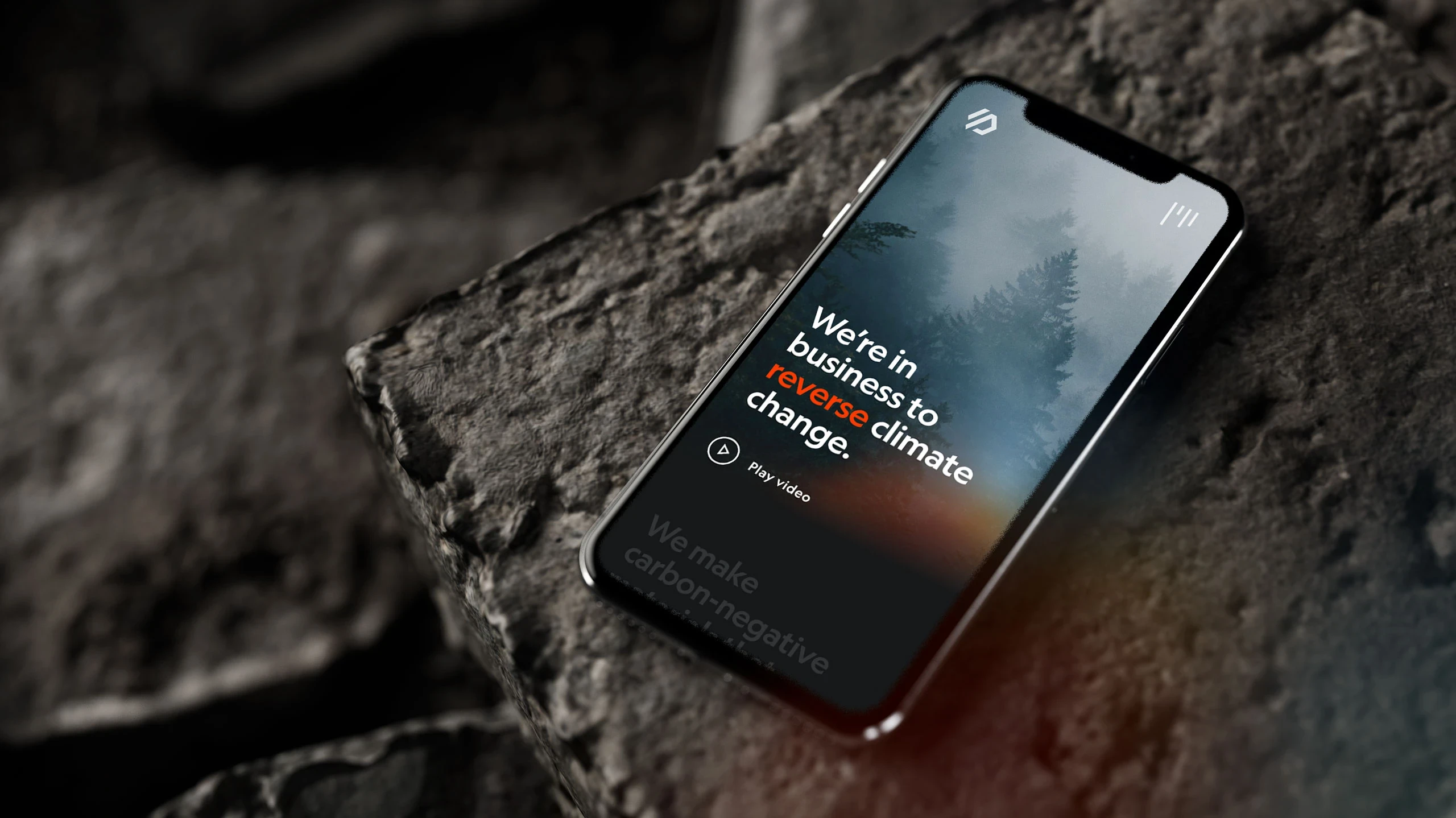 The site's mobile homepage on a phone resting on rough black rock, an orange gradient bleeding off the screen into the scene