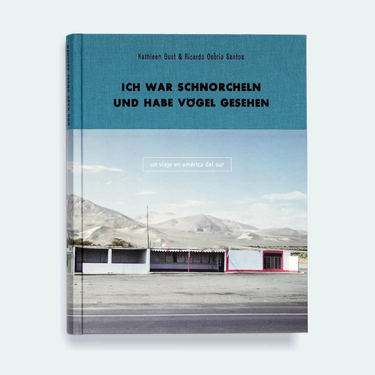 The hardback cover of Ich war schnorcheln und habe Vogel gesehen by Kathleen Gust and Ricardo Osorio Santos, teal cloth over a photograph of a roadside row of shops below bare Peruvian mountains