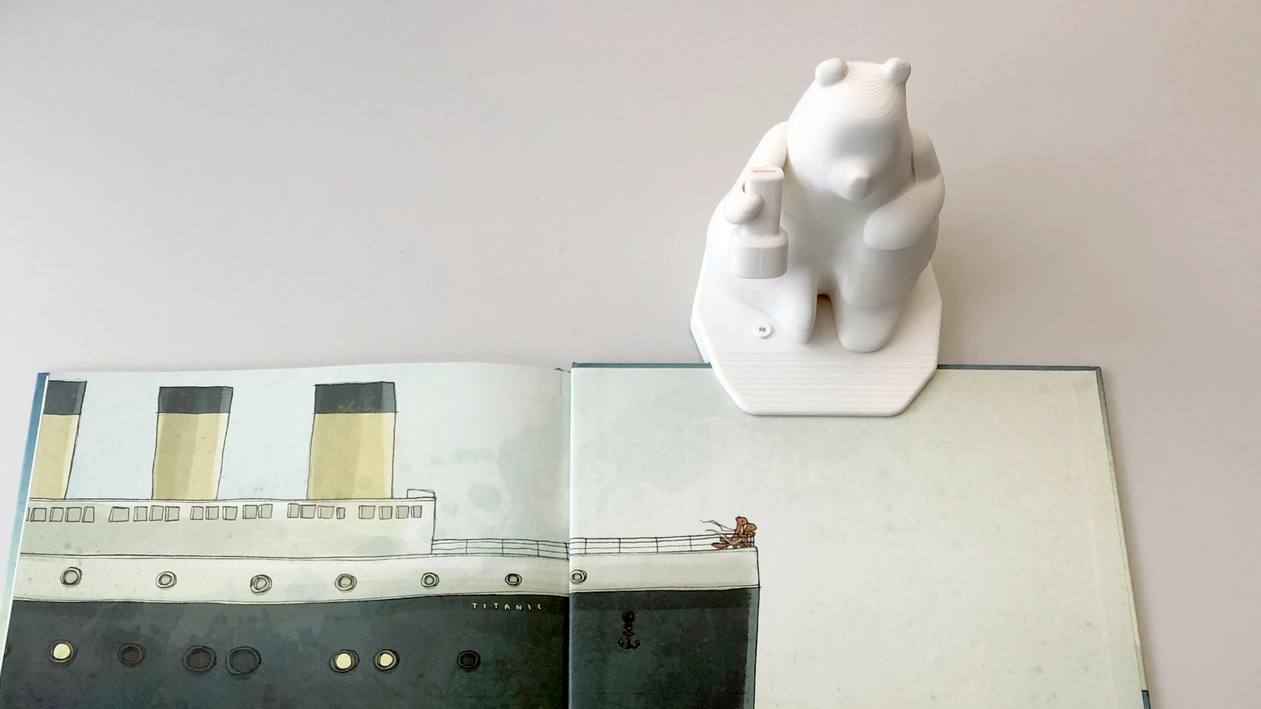 A white 3D-printed Milo clamped to the edge of an open book, testing how the device grips the page