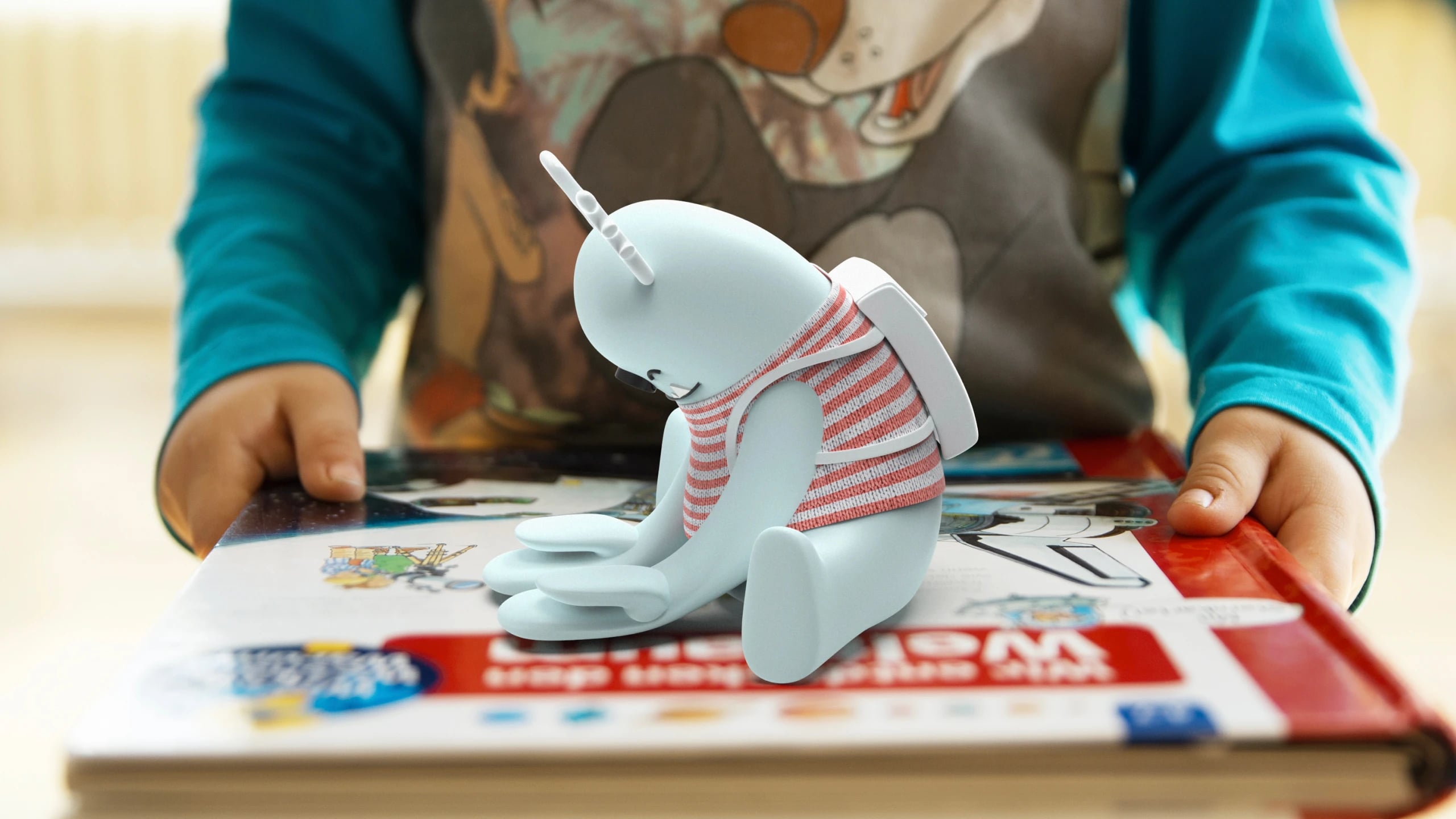 A child holding an open book with the Kit prototype sitting in the gutter of the spread