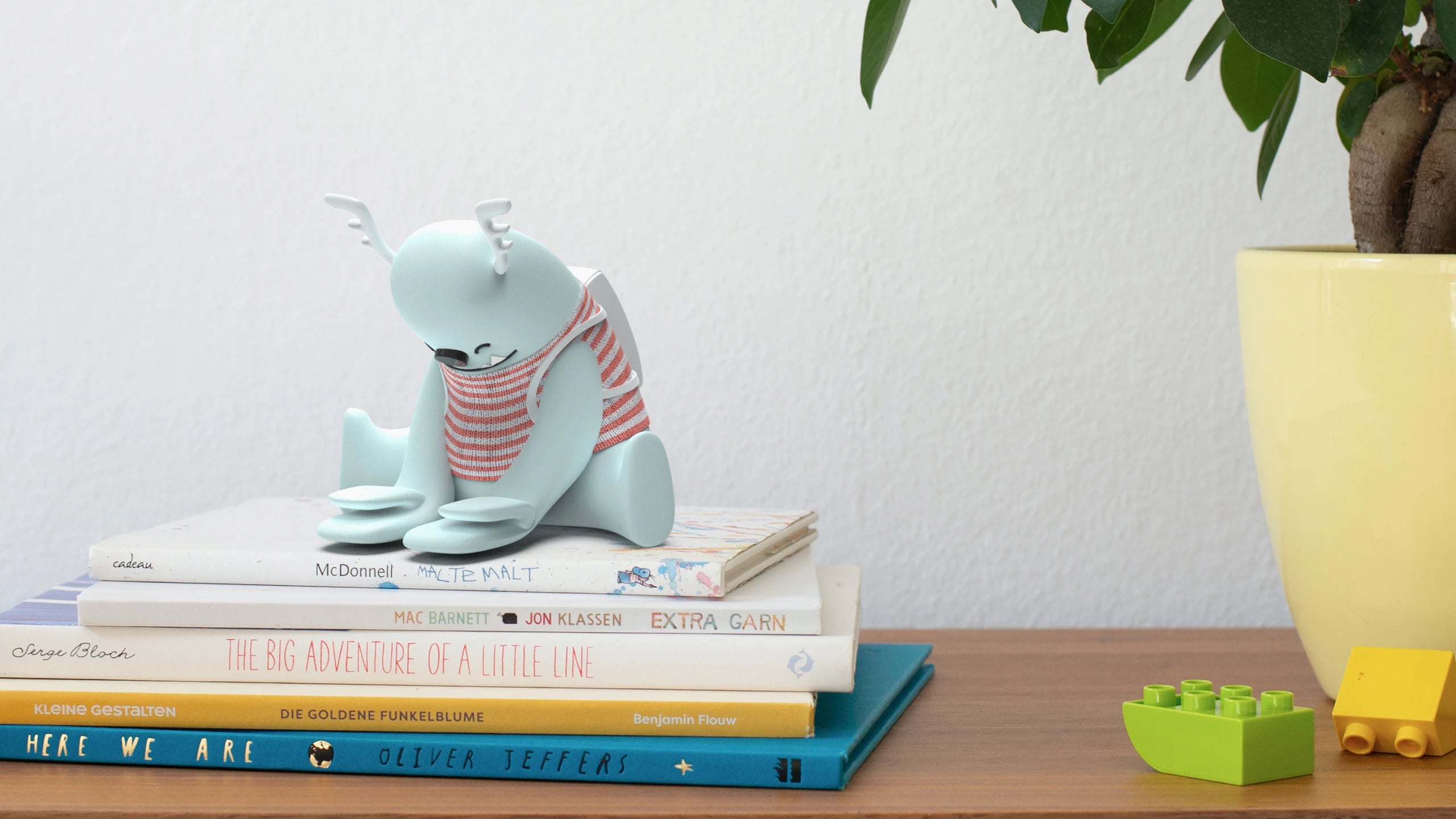 The Kit model sitting on a stack of children's books beside a yellow plant pot and two Lego bricks