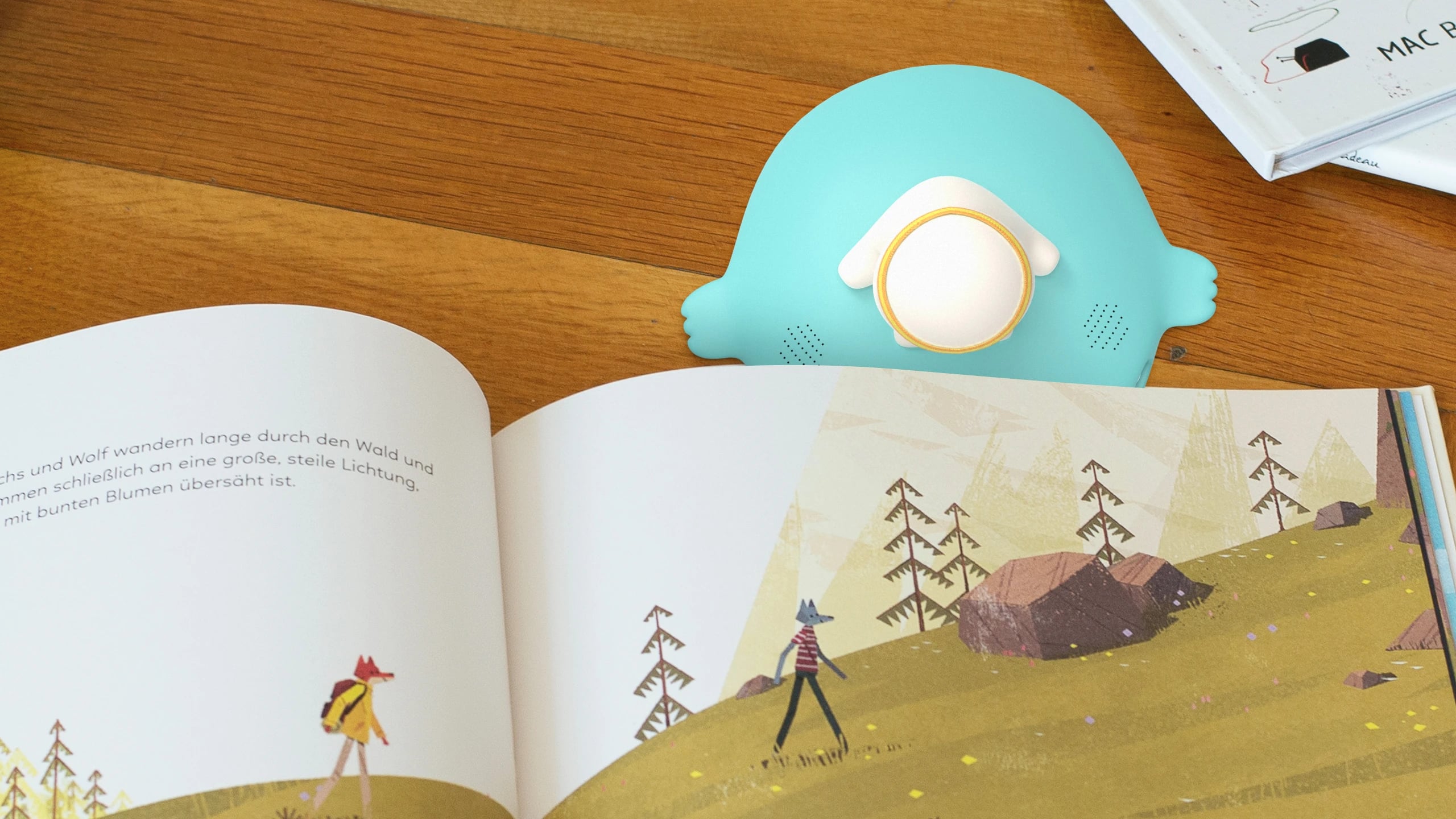 The Maya prototype sitting in the gutter of an open picture book, seen from above on a wooden table